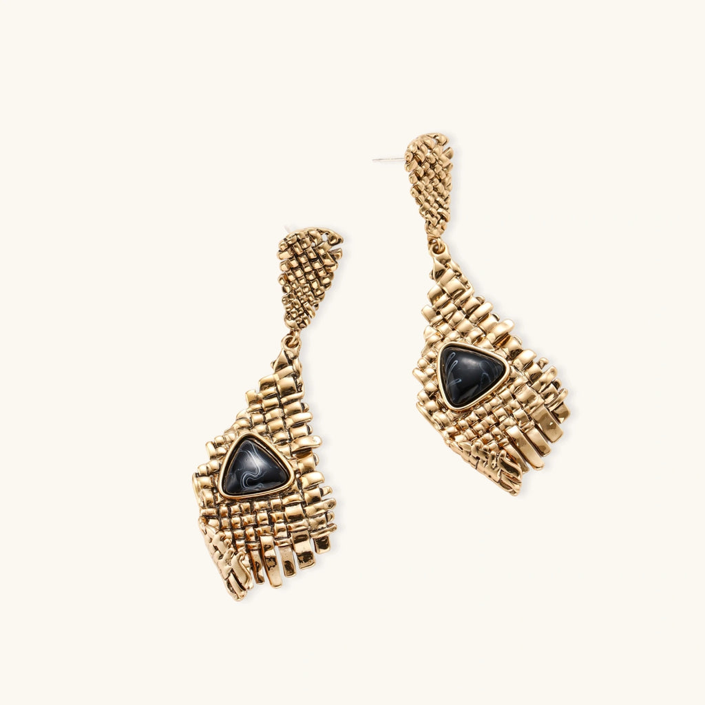 Gold-toned geometric mesh earrings with black triangular resin stones and fringe detail on neutral background