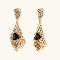 Gold-toned geometric mesh earrings with black triangular resin stones and fringe detail on neutral background