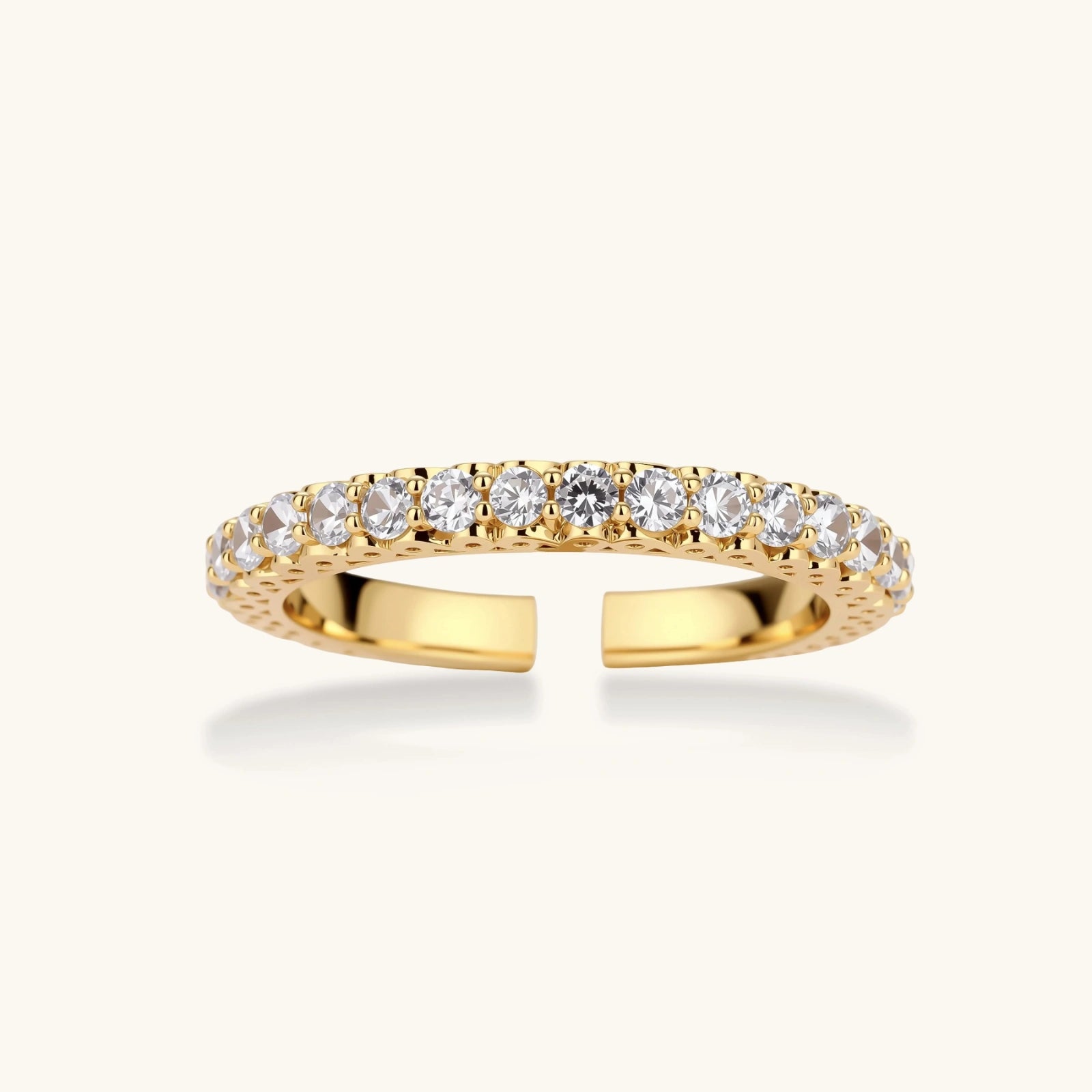 Close-up of adjustable gold-plated ring with continuous row of round zirconia stones on neutral background.