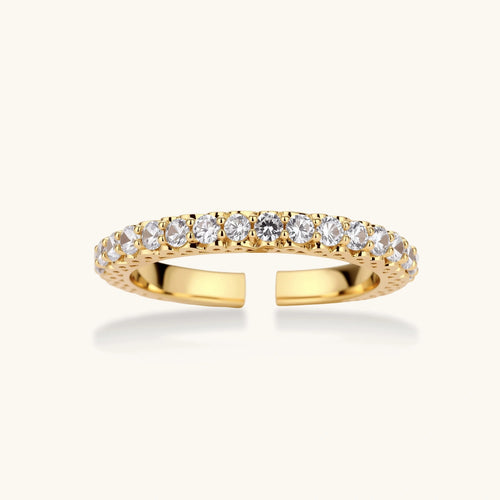 Close-up of adjustable gold-plated ring with continuous row of round zirconia stones on neutral background.