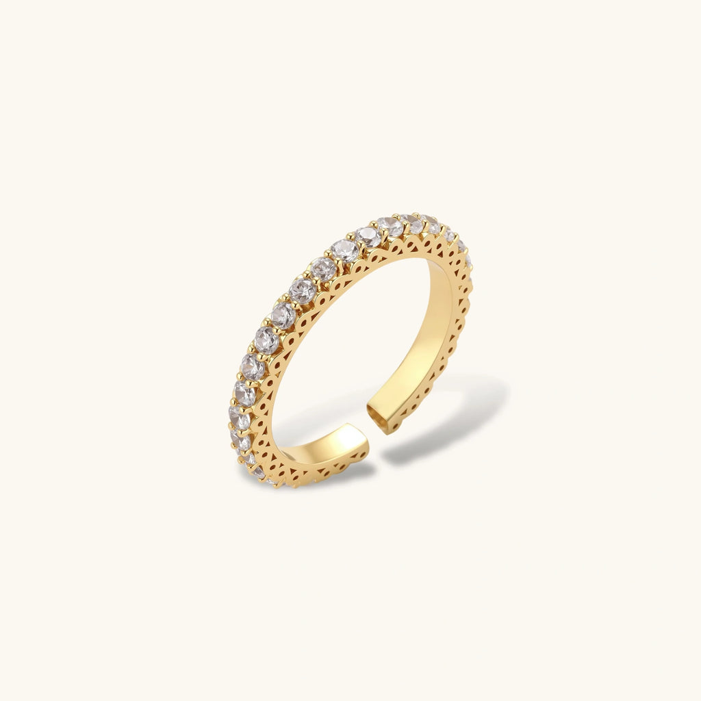 Close-up of adjustable gold-plated ring with continuous row of round zirconia stones on neutral background.