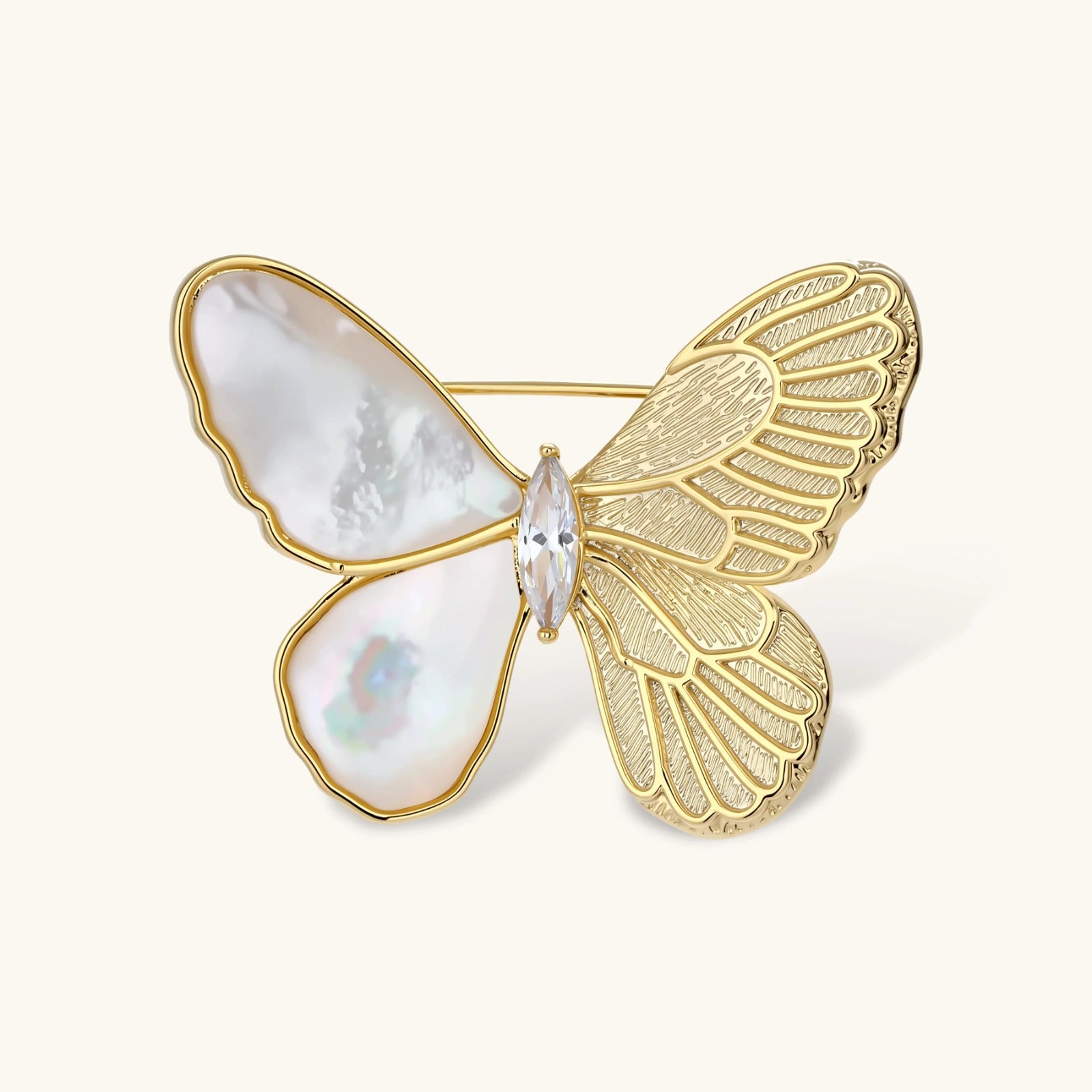 Gold-plated butterfly brooch with mother-of-pearl left wings, engraved gold right wings, and central zirconia crystal on cream background.