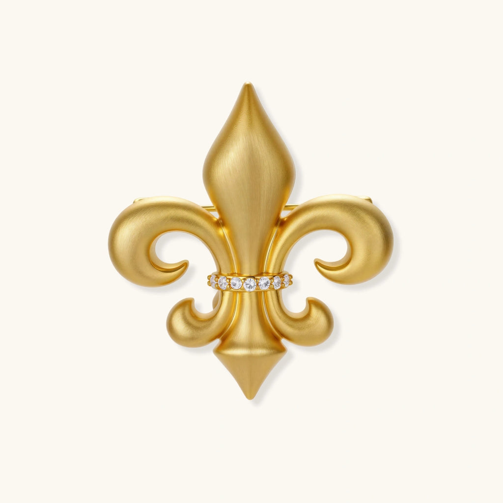 Ornate gold-plated fleur-de-lis brooch with crystal band detail on white background, showing brushed metal finish.